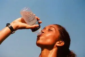 Woman drinking water from a bottle against a blue sky