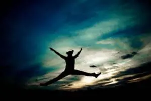 Silhouette of a person jumping with arms raised against a colorful sunset sky