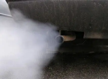Exhaust fumes billowing from a vehicle's tailpipe onto pavement