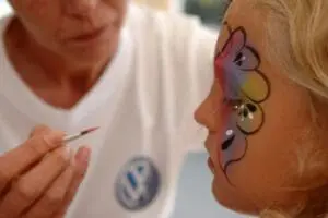 Face painter applying colorful butterfly design to woman's cheek