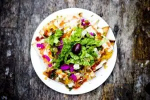 Colorful vegetarian nachos topped with greens, olives, and purple cabbage on a white plate