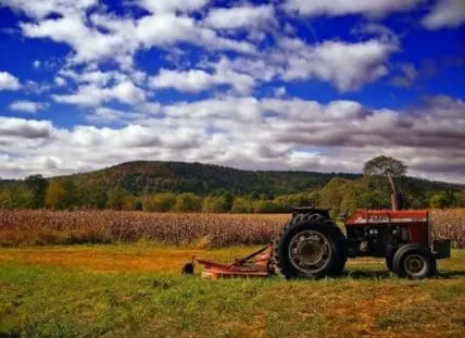 Red tractor with hay baler in cotton field with forested hills beyond