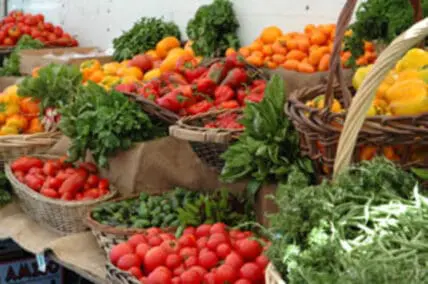 Fresh produce display at farmers market with tomatoes, peppers, and leafy greens