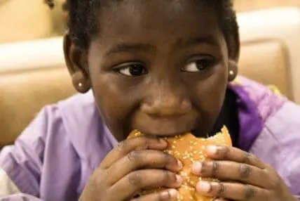Child in purple shirt eating a sesame seed burger