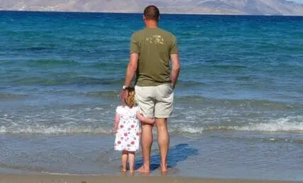 Father and daughter wading in the ocean together at the beach.