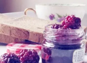 Sliced bread, jam jar, and fresh raspberries on a table with a floral teacup