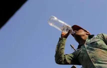 Man drinking from a plastic bottle against a blue sky