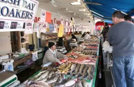 Fish market vendor displaying fresh seafood at counter with customers shopping
