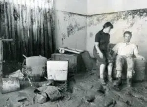 Flooded home interior with two people surveying water damage and debris