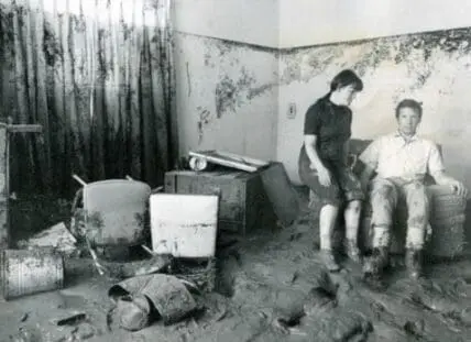 Flooded home interior with two people surveying water damage and debris