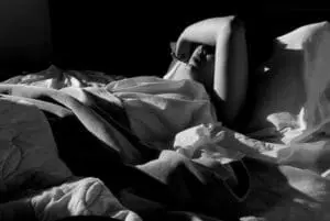Person in bed under blankets holding tissues while sick