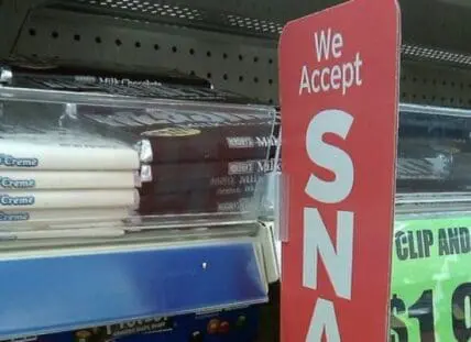 Red sign reading "We Accept SNAP" displayed in store with packaged food products on shelves