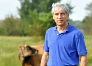 Francis Thicke standing in a field with a dog behind him