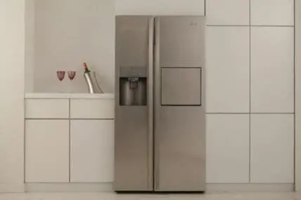 Modern stainless steel refrigerator with side-by-side doors in a minimalist white kitchen with wine