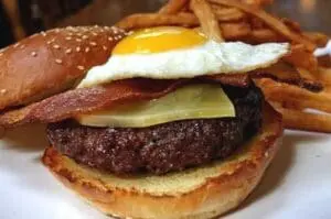 Gourmet hamburger topped with fried egg, bacon, and cheese, served with fries