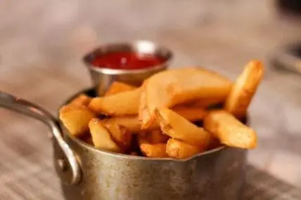 Golden french fries in a metal cup with ketchup sauce in background