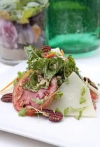 Salad with sliced cured meat, cheese, greens, and pecans on a white plate