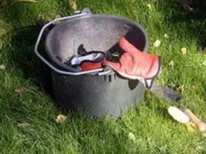 Gardener's hands holding soil and tools over a bucket on grass