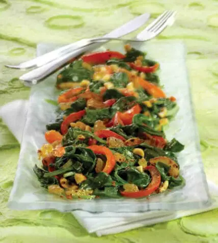 Spinach salad with red bell peppers and corn on a white plate