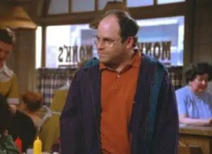 Man with glasses wearing orange shirt and navy jacket in indoor setting