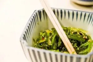 Seaweed salad in a striped bowl with wooden chopsticks