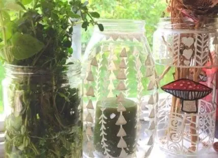 Hand-etched glass jars with tree and geometric designs displayed on a sunny windowsill
