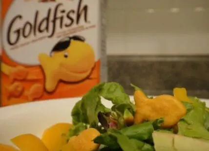 Goldfish crackers box next to a salad with greens and croutons