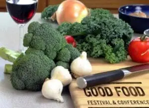 Fresh vegetables and wine displayed on a cutting board labeled "Good Food Festival & Conference