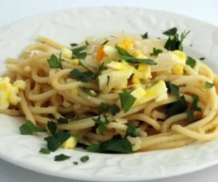 Spaghetti topped with diced boiled egg, fresh herbs, and grated cheese on a white plate