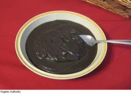 Dark chocolate spinach vegan pudding in a white bowl with a spoon on red background