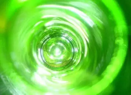 Bright green swirling liquid viewed from above, creating concentric circular ripples and light