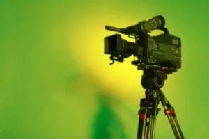 Professional video camera mounted on tripod against green background