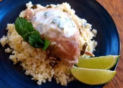 Grilled chicken with minty yogurt sauce served on couscous with lime wedges