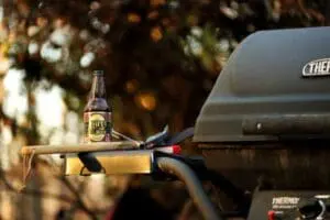 Beer bottle and grill tool on a Thermos grill shelf outdoors