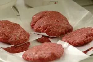 Raw ground beef patties on white paper
