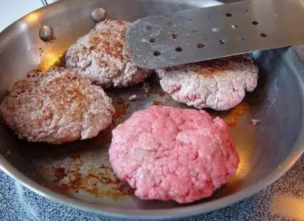 Raw ground beef patties cooking in a stainless steel skillet