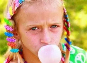 Child blowing a pink bubble with colorful braided hair clips