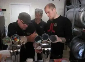 Three brewers examining beer samples in a home brewing setup