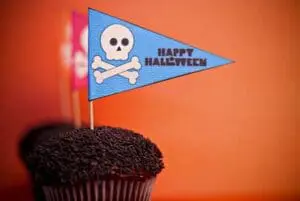 Chocolate cupcake topped with dark frosting and a blue pirate flag decorated with a skull and