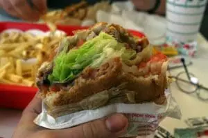 Overstuffed fast food burger with lettuce and sauce being held in wrapper