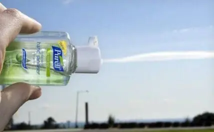 Hand sanitizer bottle held up outdoors against a clear sky
