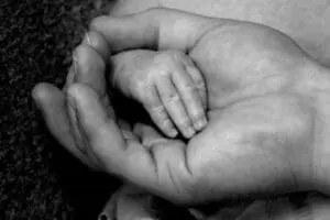 Baby's hand resting on adult's palm in black and white