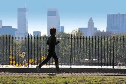 Runner jogging along fence with city skyline in background