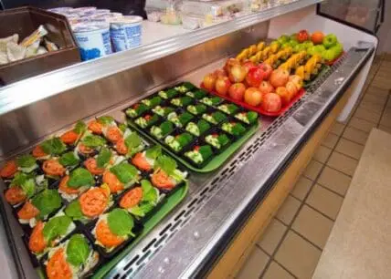 Refrigerated display case with fresh vegetables and prepared salads in a school cafeteria