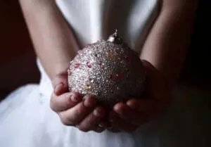 Child's hands holding a glittery red and silver Christmas ornament