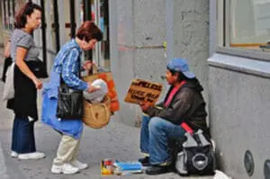 A person giving money to a person sitting on the street with a cardboard sign