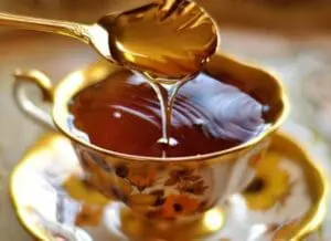 Golden honey substitute dripping from a wooden spoon into a decorative teacup