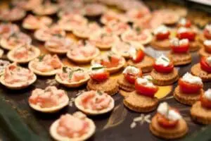 Assorted appetizers on black platter including crostini with toppings and crackers with cheese and