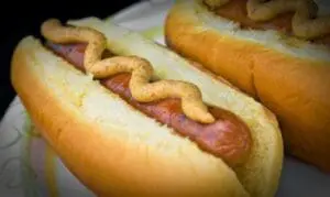 Two hot dogs with mustard on a white plate