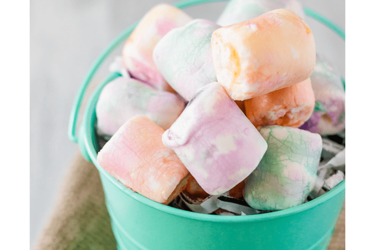 Image of colorful dyed and tie-dyed marshmallows piled up in a teal, metal bucket for Easter. By reading this article, you'll learn a super simple way for coloring marshmallows that come out so pretty. And easy and fun craft with a tasty result.